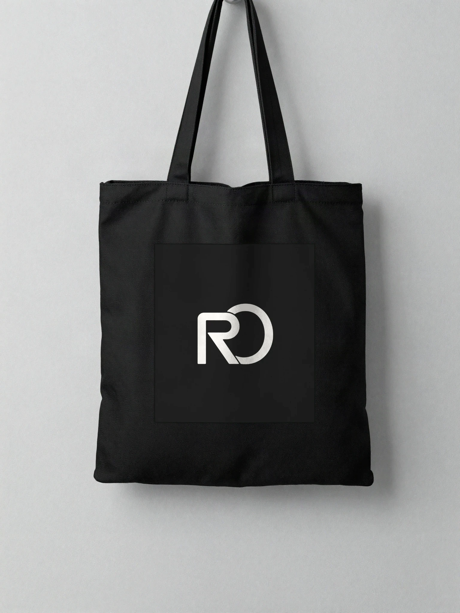 Black tote bag with the RO mark hanging on a light wall